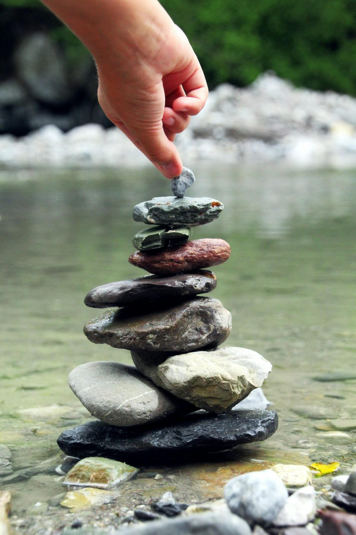 A hand stacking rocks into a balanced tower in a peaceful river